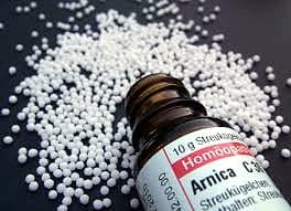 Ein Fläschchen Arnica als homöopathisches Einzelmittel, daneben verstreute Streukügelchen (Globuli)