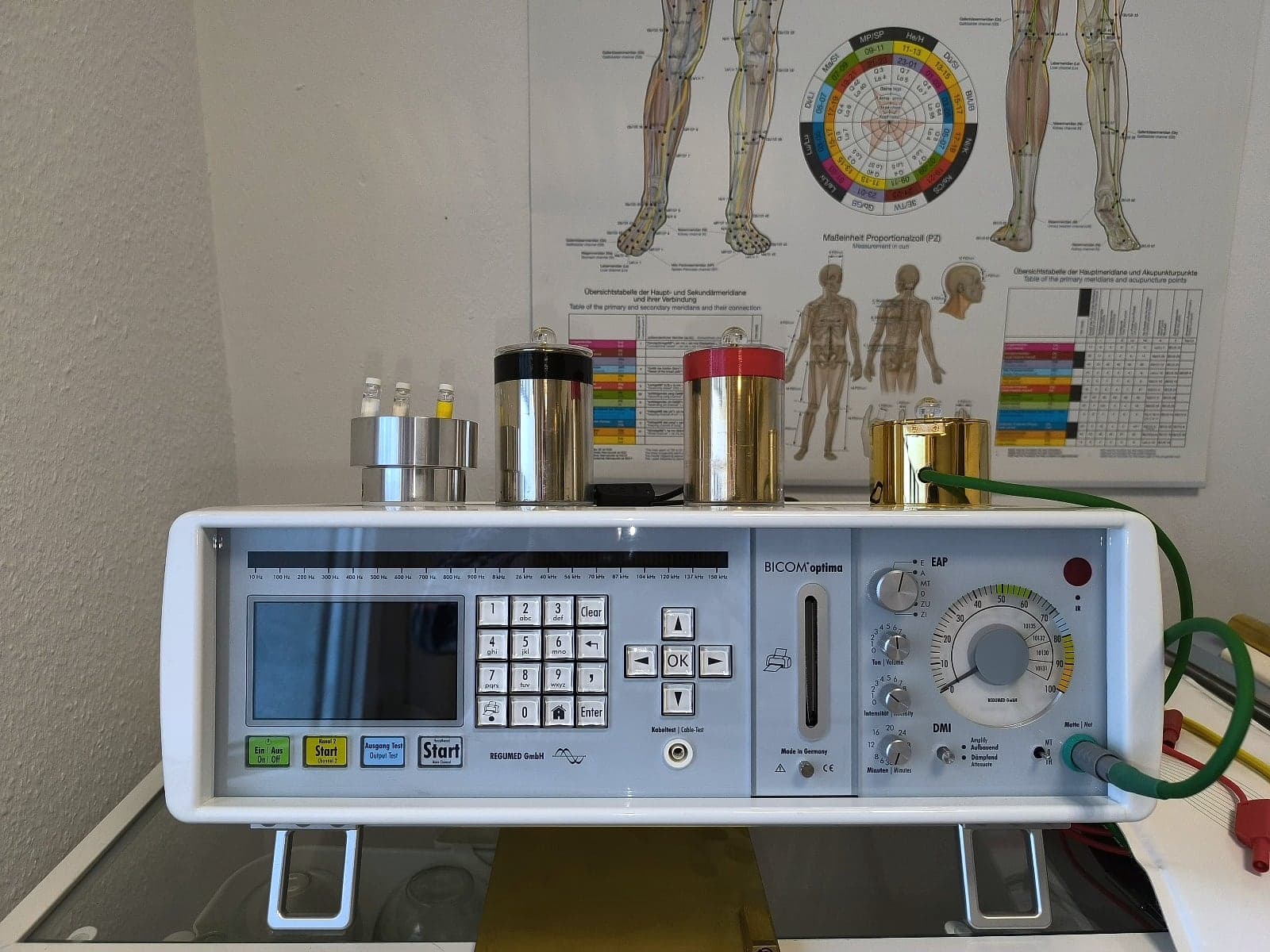 Das Bioresonanzgerät BICOM Optima in der Naturheilpraxis Karra, dahinter eine Tafel mit den Haupt- und Sekundärmeridianen